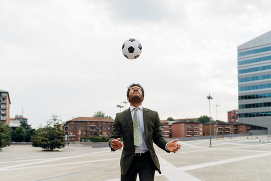 Businessman heading the ball while playing in city