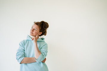 Pensive casual woman touching her face with a finger, lost in thought and gazing away on a clean...