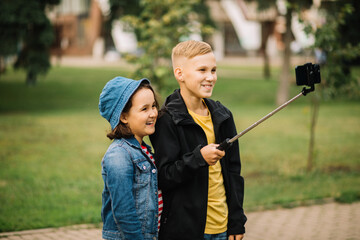 Girl and boy teenagers bloggers influencer records videos from the blog on a smartphone outdoor. Kids have fun with online live streaming for social network.
