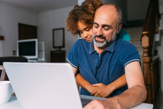 Girl embracing father using laptop working from home