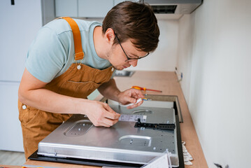 Professional electrician carefully connecting wires to a new electric stove during installation in a modern kitchen, ensuring proper electrical connections for safe and efficient operation