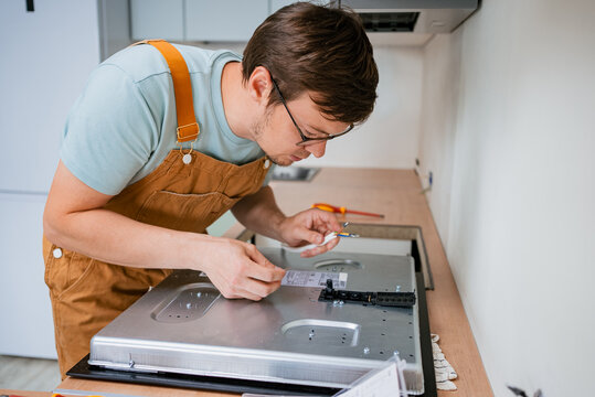 Professional electrician carefully connecting wires to a new electric stove during installation in a modern kitchen, ensuring proper electrical connections for safe and efficient operation - Powered by Adobe
