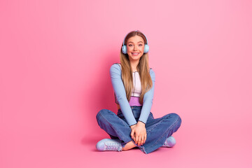 Charming young woman with headphones enjoying leisure time against a pastel pink wall, showcasing...