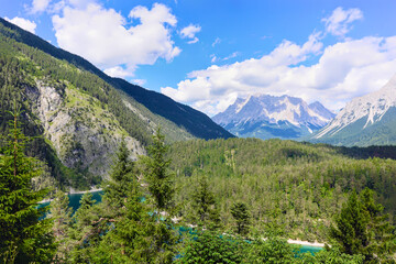 Breathtaking panoramic view of alpine forest, turquoise lake, and rugged mountain peaks under a...