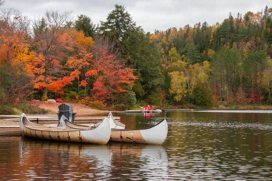 Two canoes on lake in Canada Algonquin in fall Autumn with reflections and reds orange and yellow leaf colours