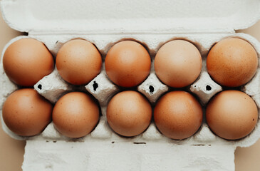 Brown eggs in white carton on beige background flat lay