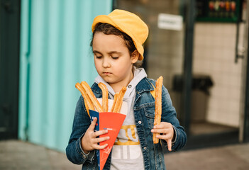 Cute little girl eating traditional Spanish treat street fast food churros. Food delivery or take away food concept.