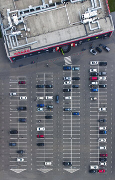Kharkiv, Ukraine - 06 June 2021: Aerial view of a supermarket with its parking lot filled with cars, casting shadows on the grey asphalt.