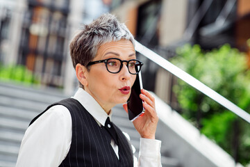 Confident mature businesswoman speaking on a mobile phone outdoors, showcasing professional attire...