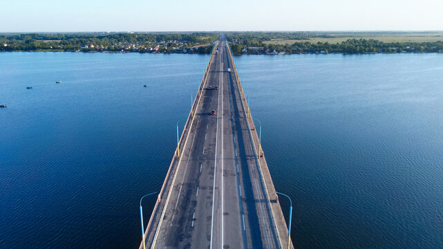 Aerial view of the Antonovsky Bridge stretching across the tranquil, deep blue waters, connecting distant shores under a clear sky, Kherson, Kherson Oblast, Ukraine.