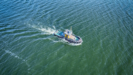 Kherson, Ukraine - 17 September 2021: Aerial view of a tugboat slicing through the dark, rippled waters, leaving a frothy white wake against the deep blue-green hues of the sea.