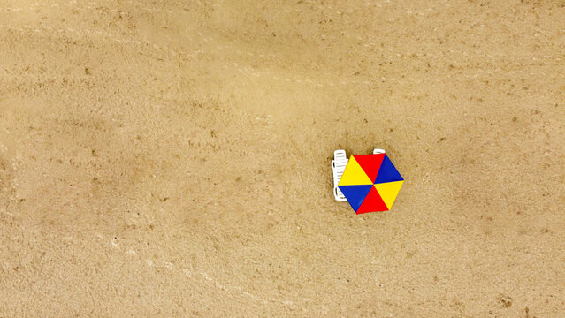 Aerial view of a striking, colorful beach umbrella standing out against the sandy expanse, creating a vivid contrast of textures and tones, Kherson Oblast, Ukraine.