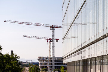 Real estate development in progress with cranes and glass building facade in contemporary district, highlighting construction industry and city expansion infrastructure.