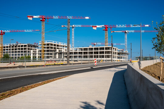 Wide city street surrounded by construction cranes and emerging buildings, showing progress in infrastructure and real estate investment in modern urban environments.