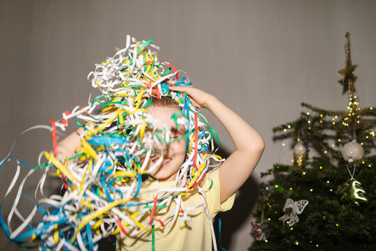 Cheerful boy playing with party poppers near Christmas tree at home