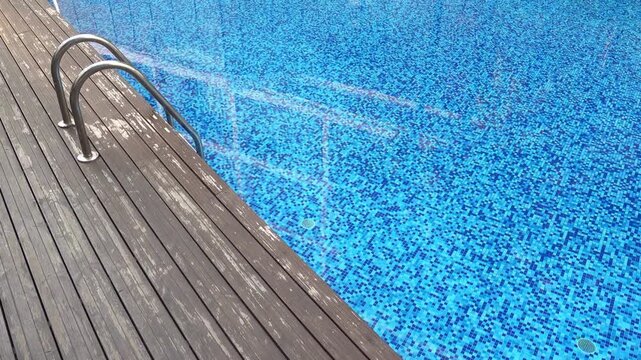 Swimming pool with blue tiles and wooden deck on a sunny day