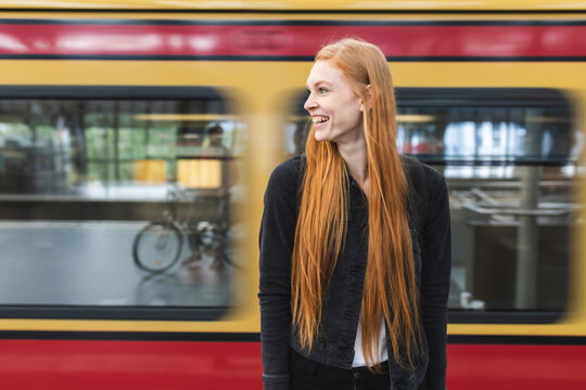 Laughing redheaded young woman waiting at platform, Berlin, Germany