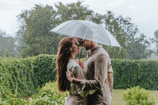 Romantic couple standing with umbrella in rain at garden