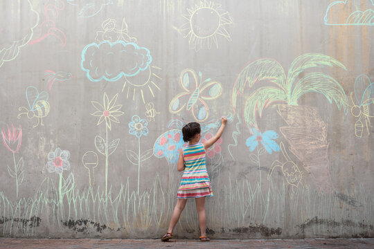 Girl drawing colourful pictures with chalk on a concrete wall
