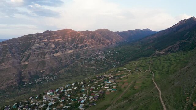 Aerial view of houses nestled between majestic mountains, a rugged landscape with a winding road cutting through the green terrain, Goor, Republic of Dagestan, Russia.