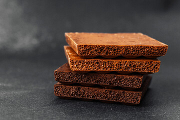 Stack of milk chocolate pieces with aerated texture on dark background