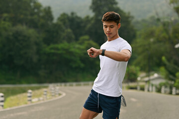 An Athletic Asian male runner timing his warm-up while stretching his quad before a workout