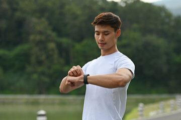 An Asian Man standing outdoors, focusing on his smartwatch to track exercise time before running