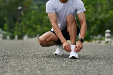 Close-up of an athlete tying running shoes on an asphalt road, getting ready for outdoor exercise