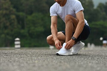 Close-up of an Asian Male runner crouching and adjusting his shoelaces before starting a fitness...