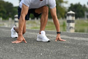 Close-up of a male athlete in starting position for a sprint, hands on the ground, ready to run on...