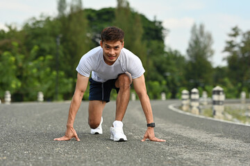 An Asian Male runner in a sprint start position, focused and prepared for outdoor running exercise...