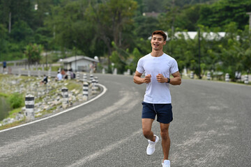 A Young Asian man jogging on an open road in a natural environment, promoting health, fitness, and an active lifestyle