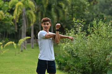 An Asian Athletic man stretching arm outdoors in a green park, preparing for exercise or workout