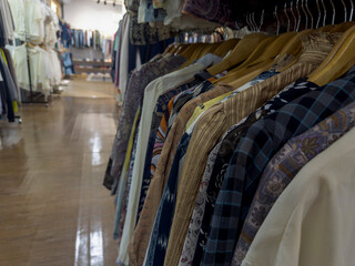 A clothing rack filled with a variety of patterned and plain shirts hangs in a well-lit store with other clothing displays in the background.