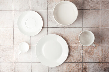 Assorted white ceramic tableware set on rustic tile background flat lay
