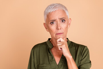 Charming mature woman with short white hair wearing a khaki green shirt, posing against a beige...