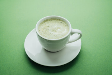 Matcha latte in white cup on green table close up