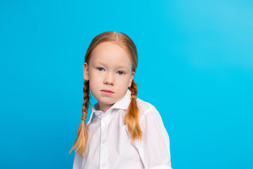 Portrait of a young girl with braided red hair against a vibrant blue background, wearing a white...
