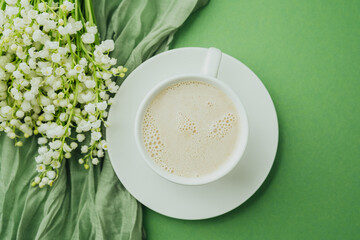 Cup of coffee with milk and lily of the valley flowers on green textile background