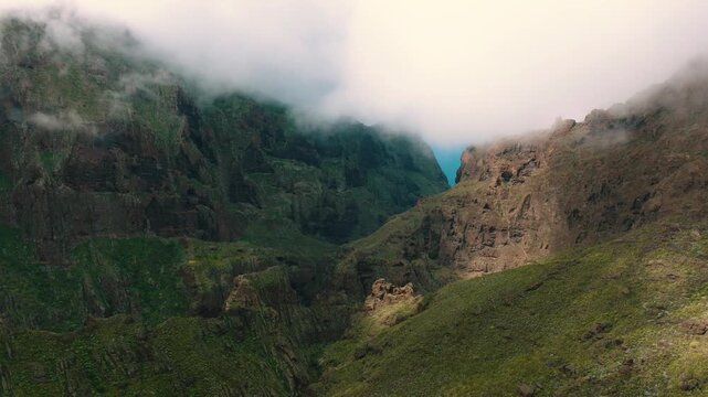 Aerial view of Masca village gorge opening to the turquoise ocean through dramatic cliffs and clouds, Tenerife, Canary Islands