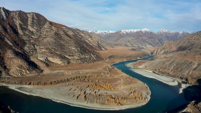 Aerial view of the winding river cutting through the rugged mountains, contrasting the blue water with the earthy tones of the landscape, Ulagan, Altai Republic, Russia.