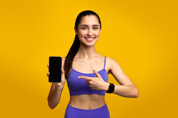 Fitness Application. Portrait of smiling slim young woman in sportswear holding mobile phone and...
