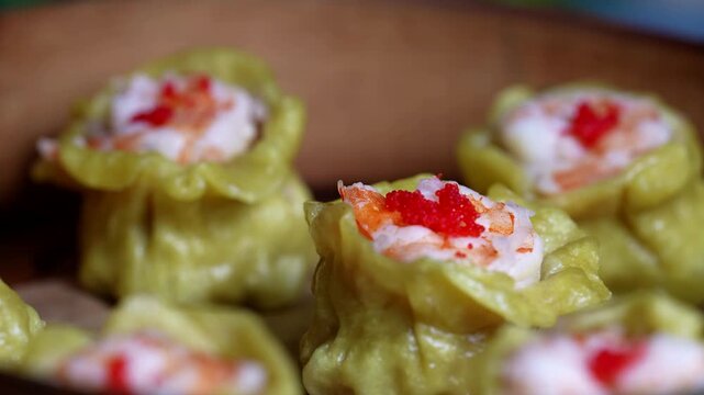 Bright green sushi rolls with rice, cream cheese, tuna, and flying fish roe on a black plate.