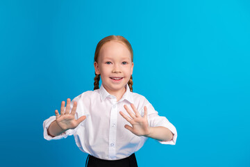 Smiling schoolgirl with red braided hair making hand gestures against a blue background emphasizing...