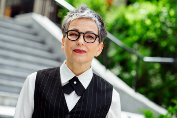 Confident mature businesswoman in urban setting wearing formal attire under sunny outdoor...