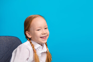 Smiling young girl with red hair and braids in a white shirt against a vivid blue background...
