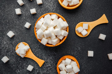 Sugar cubes arranged in wooden bowls and spoons on dark surface