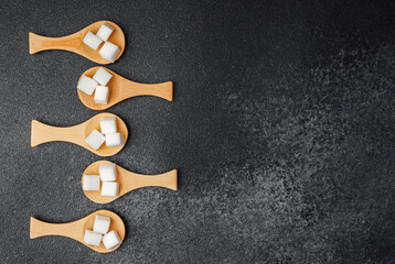 Spoonfuls of sugar on wooden spoons arranged on a dark surface
