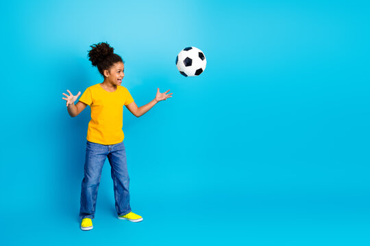 Adorable girl standing against a vibrant blue background catching a soccer ball with excitement and enthusiasm - Powered by Adobe