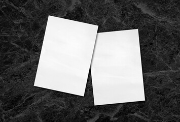 close up of white grunge paper placed on black marble background with blank space for design. empty white paper sheet on luxury stone table in top view.